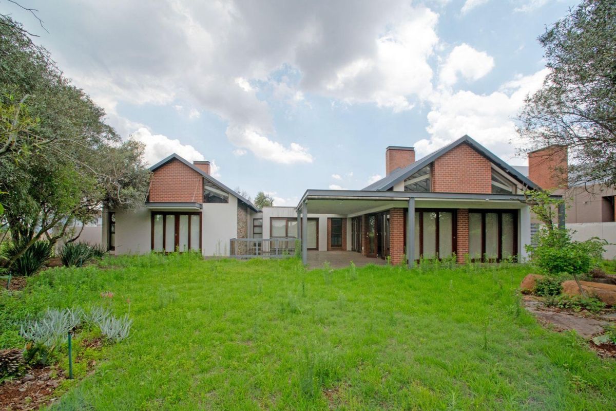 Rear view of a modern brick house featuring a covered patio, large glass doors, and an expansive garden area.