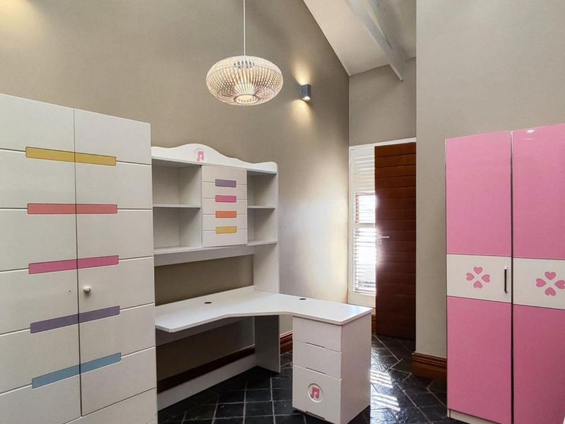 A bedroom featuring a high vaulted ceiling, dark tiled flooring, and shutter blinds, providing a bright and spacious atmosphere.