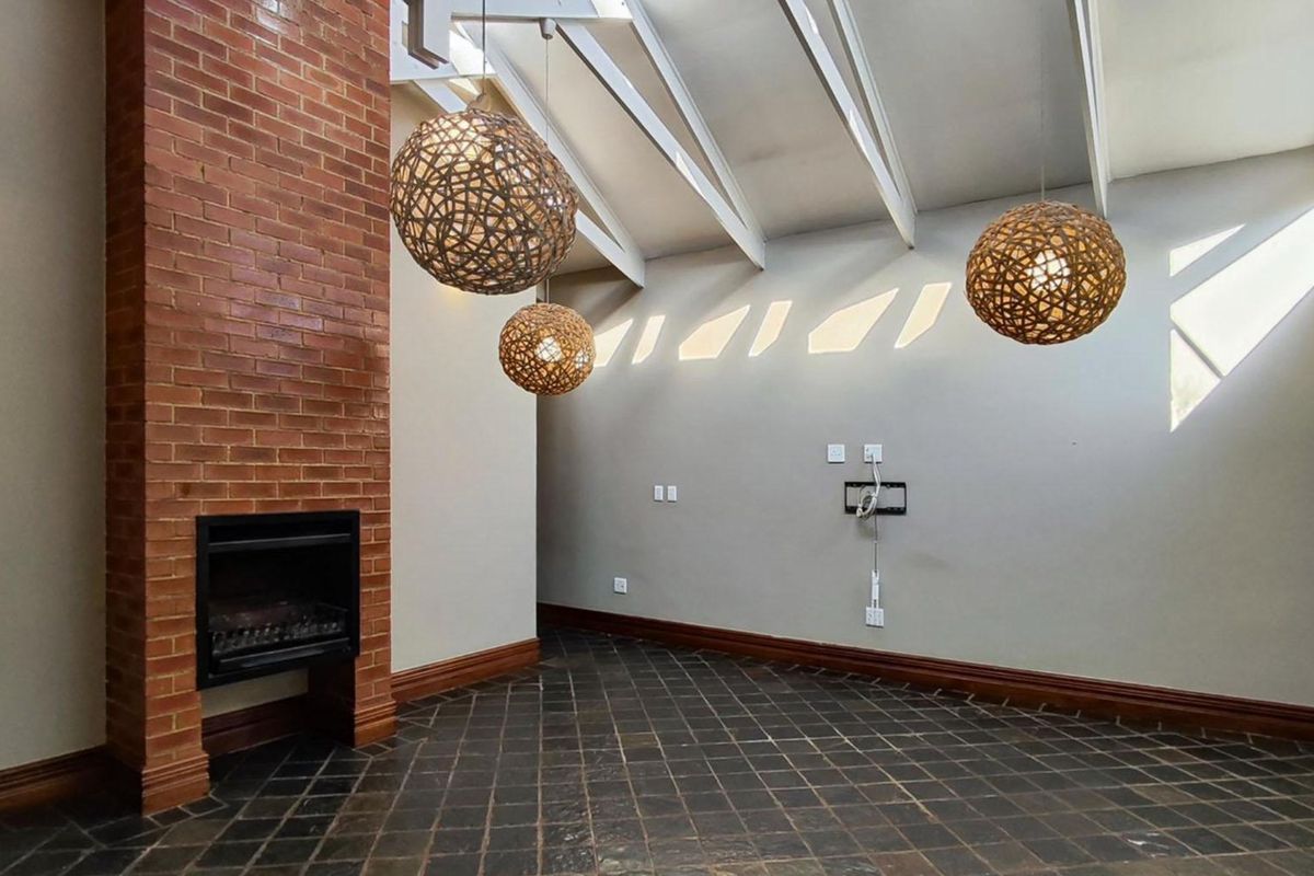Spacious living room featuring a prominent exposed brick fireplace, vaulted ceilings with exposed rafters, and dark tiled flooring.