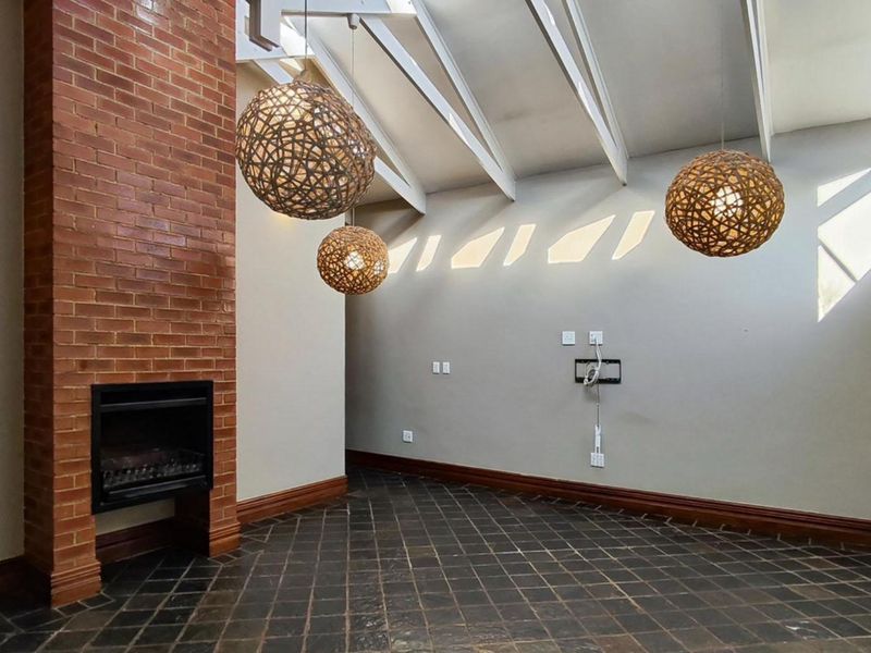 Spacious living room featuring a prominent exposed brick fireplace, vaulted ceilings with exposed rafters, and dark tiled flooring.