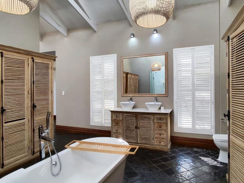 Spacious bathroom featuring a double vanity, freestanding bathtub, vaulted ceilings with exposed rafters, and elegant shutter blinds.