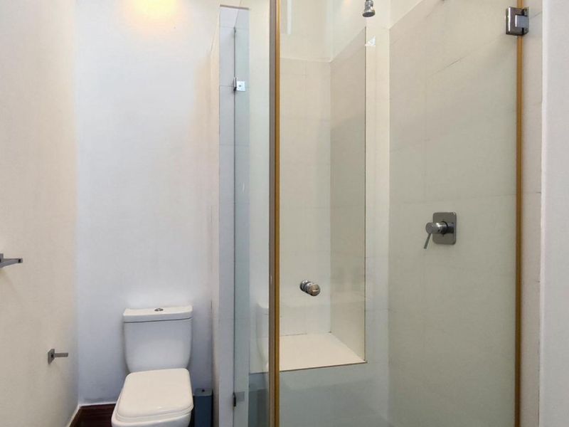 A clean, modern bathroom featuring a glass-enclosed shower, wall-mounted shower mixer, and a standard toilet.