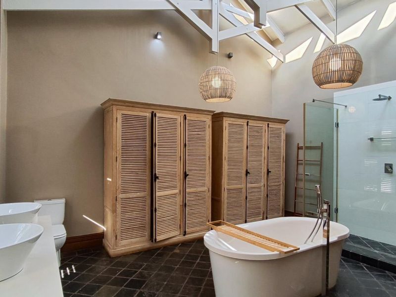 Spacious bathroom featuring a double vanity, freestanding bathtub, walk-in shower, and high vaulted ceilings with exposed trusses and skylights.