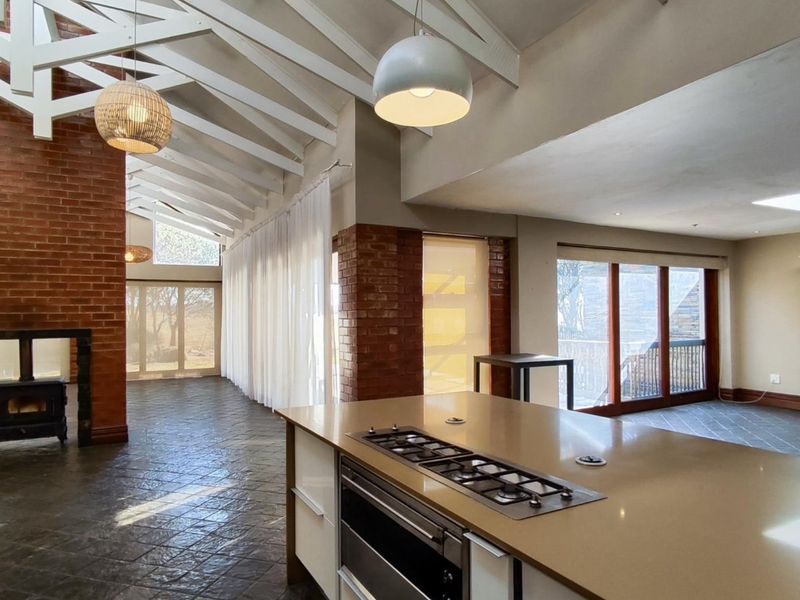 Spacious open-plan living area featuring exposed timber rafters, a brick fireplace with a wood-burning stove, and a modern kitchen island with built-in appliances.