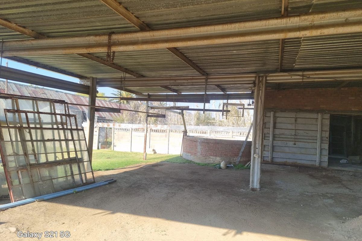 A large, open-sided covered outdoor area featuring a corrugated metal roof and steel support structure, suitable for conversion into a workshop or entertainment space.