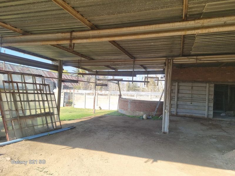 A large, open-sided covered outdoor area featuring a corrugated metal roof and steel support structure, suitable for conversion into a workshop or entertainment space.