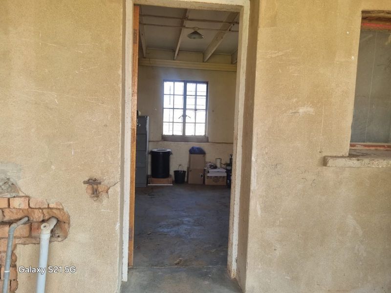 A utility space featuring exposed brickwork, concrete flooring, and exposed ceiling beams, requiring significant renovation and plaster repair.
