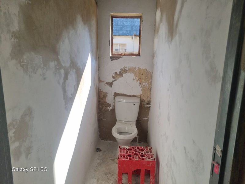 A small bathroom in a state of renovation, featuring a toilet and window, requiring significant wall finishing and cosmetic repairs.