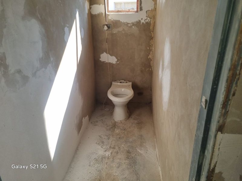 A small, unfinished bathroom space featuring a toilet, requiring significant renovation and finishing of walls and flooring.