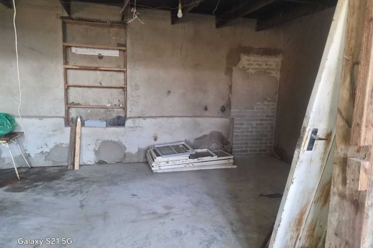 An unfinished garage space featuring exposed timber ceiling joists, concrete flooring, and built-in wall shelving, requiring significant renovation and finishing work.