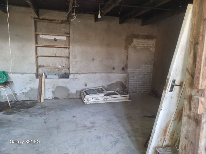 An unfinished garage space featuring exposed timber ceiling joists, concrete flooring, and built-in wall shelving, requiring significant renovation and finishing work.