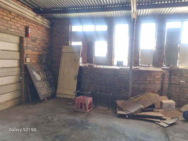 An unfinished garage space featuring exposed brick walls, a corrugated metal roof, and concrete flooring, offering potential for workshop or storage conversion.