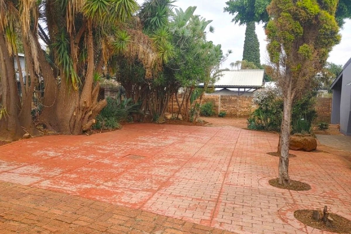 A spacious rear garden area featuring extensive brick paving, mature trees, and a brick boundary wall, offering a private outdoor space.