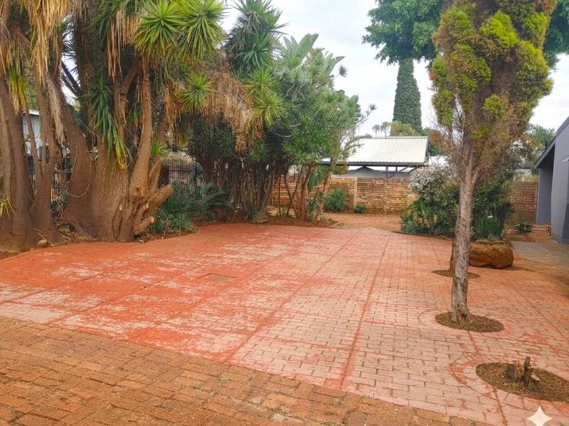 A spacious rear garden area featuring extensive brick paving, mature trees, and a brick boundary wall, offering a private outdoor space.