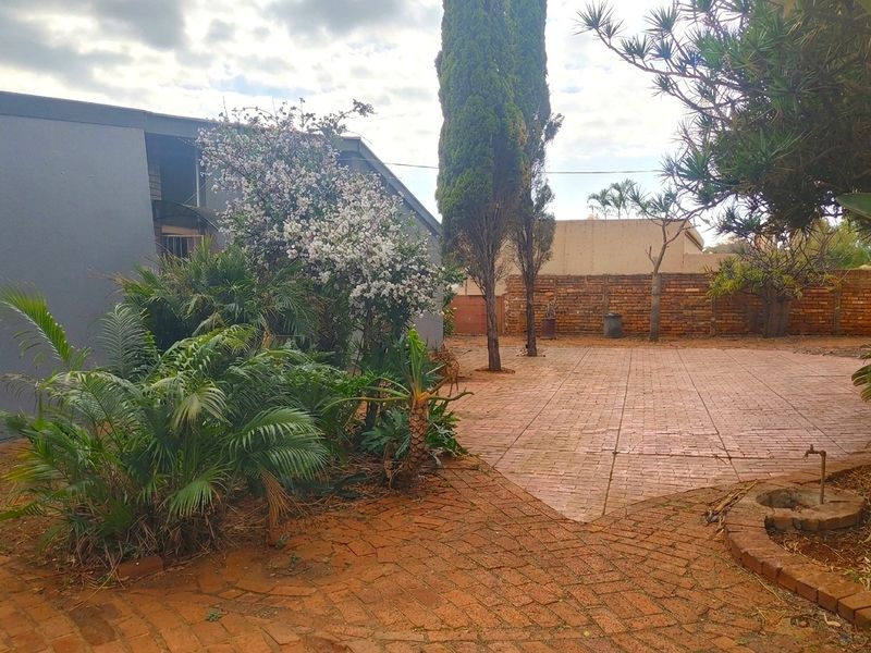 A spacious rear garden area featuring extensive brick paving, established trees, and a brick boundary wall, offering potential for outdoor landscaping and entertainment.