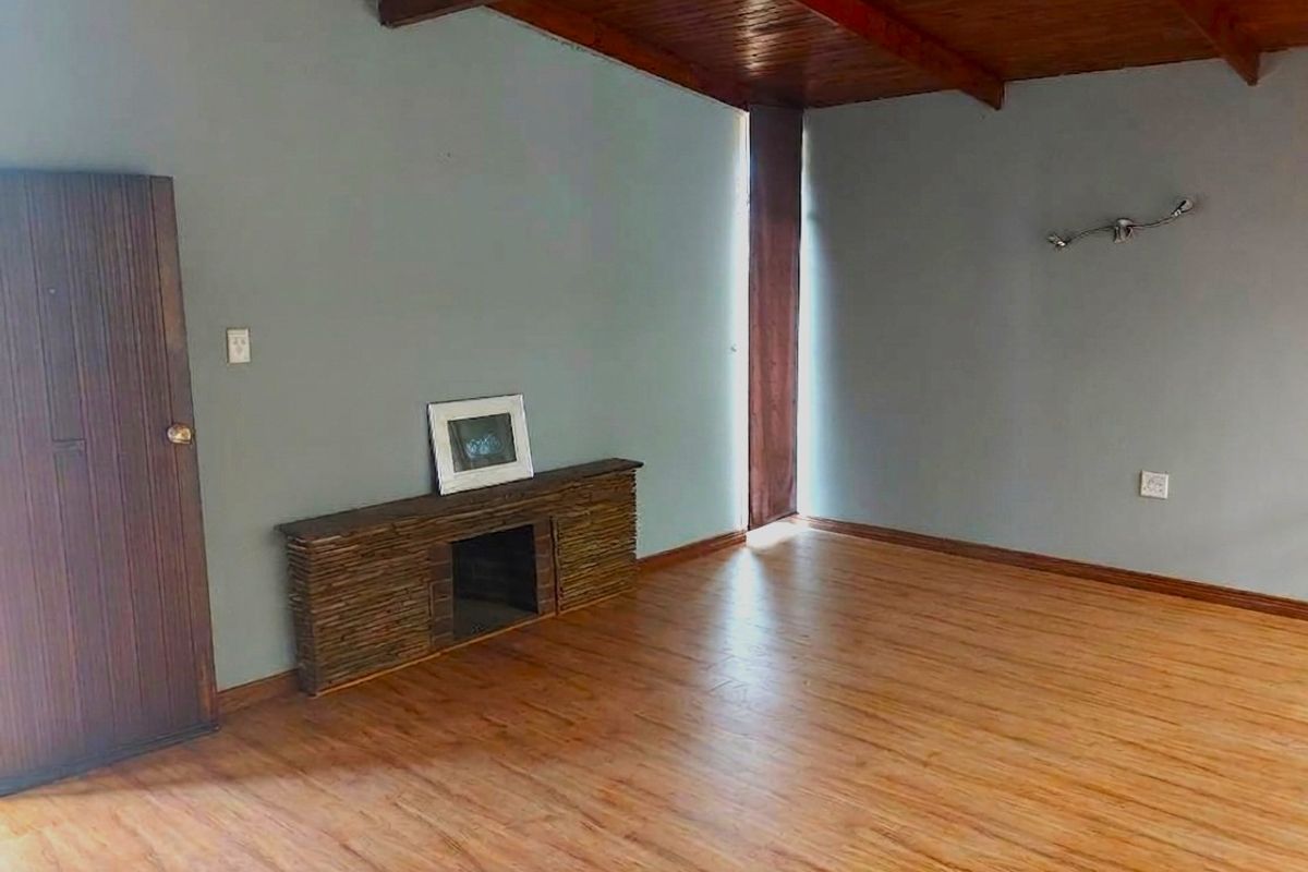 Spacious living room featuring warm laminate flooring, exposed timber ceiling beams, and a unique built-in stone-clad fireplace feature.