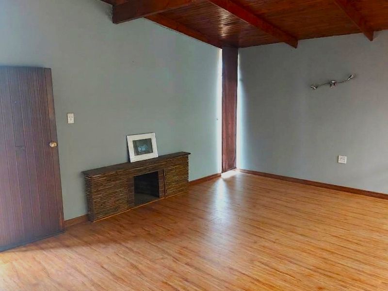 Spacious living room featuring warm laminate flooring, exposed timber ceiling beams, and a unique built-in stone-clad fireplace feature.