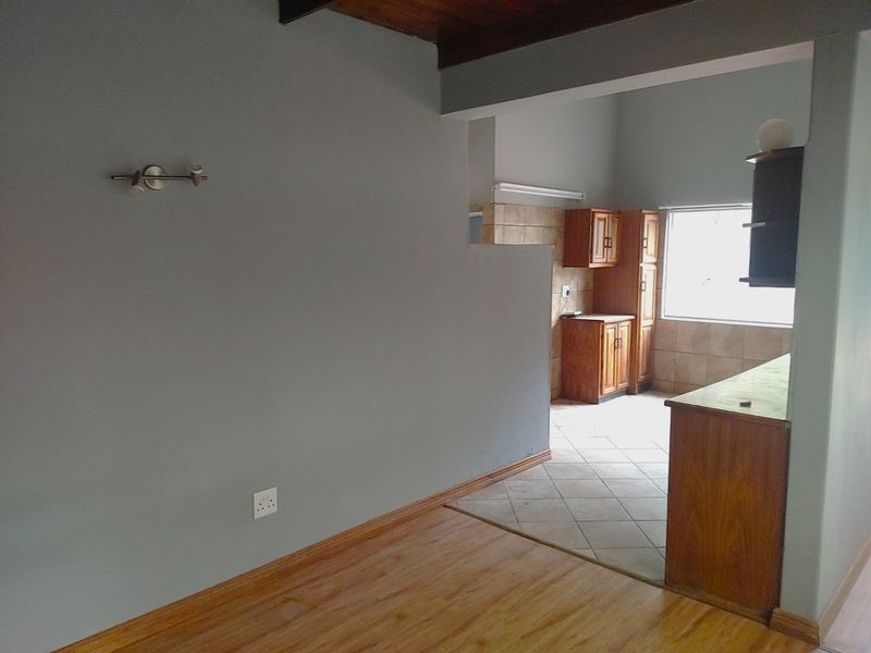 Open plan living area featuring a transition between laminate and tiled flooring, with a functional kitchen space and exposed timber ceiling beams.