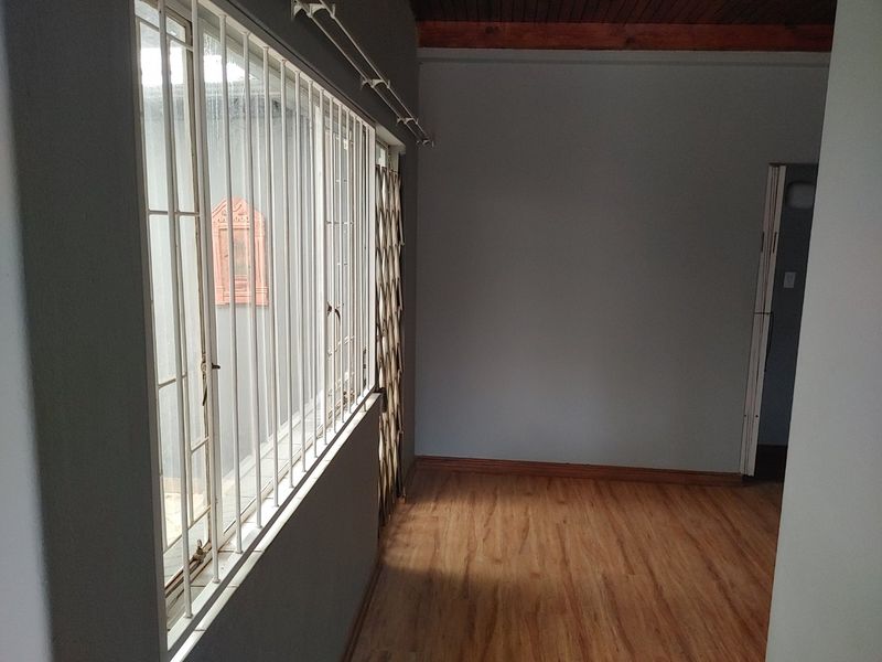 An empty living area featuring laminate flooring, timber ceiling accents, and security bars on the windows.