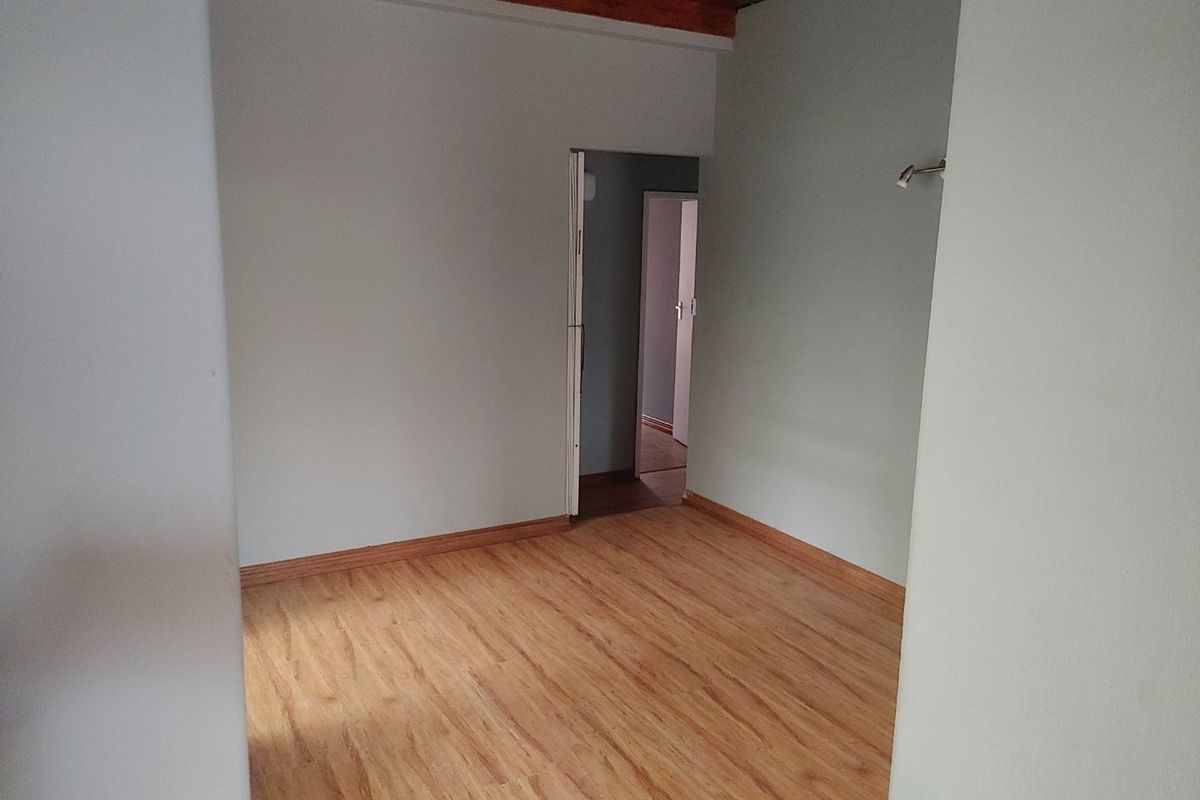An empty bedroom featuring warm-toned laminate flooring and exposed timber ceiling beams, offering a clean and neutral space ready for personalization.