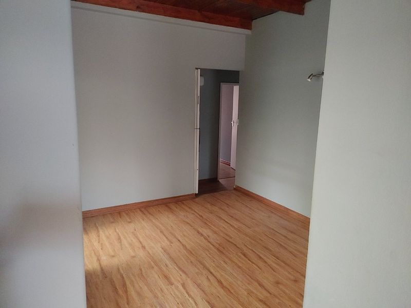 An empty bedroom featuring warm-toned laminate flooring and exposed timber ceiling beams, offering a clean and neutral space ready for personalization.