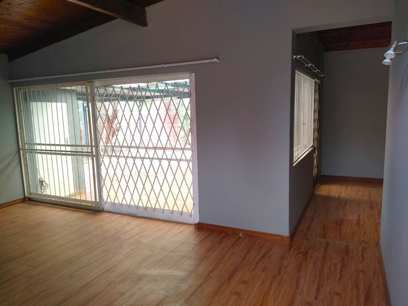 An empty living room featuring laminate flooring, exposed timber ceiling beams, and sliding glass doors with security gates leading to the exterior.