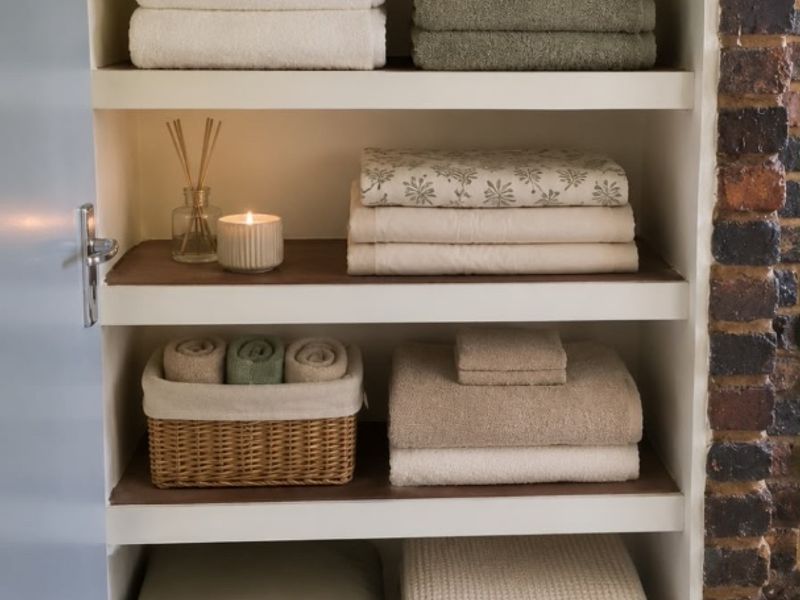A neat built-in storage cupboard featuring multiple shelves, exposed brick detailing, and tiled flooring, ideal for linen or utility storage.