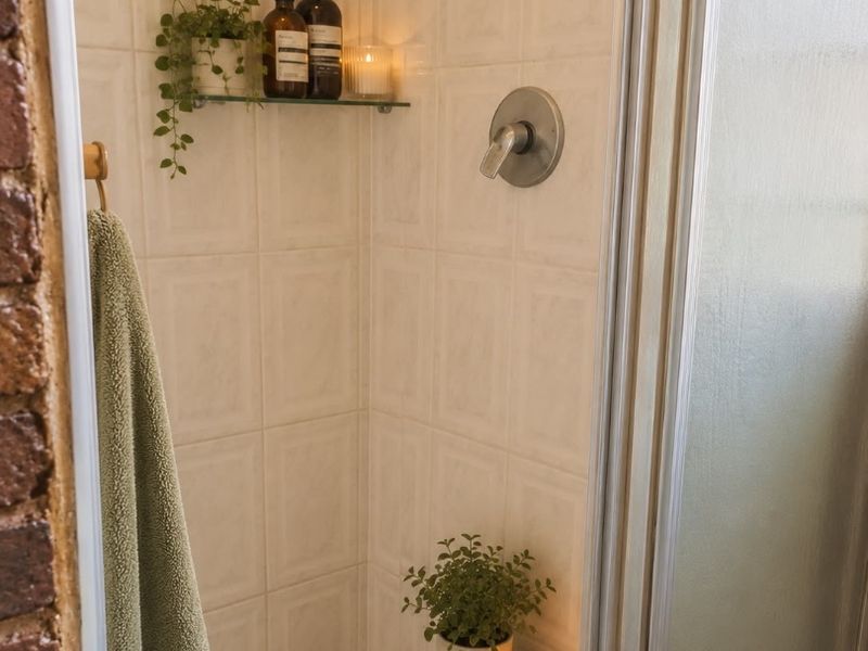 A compact shower enclosure featuring tiled walls, a glass door, and a standard shower mixer fixture.