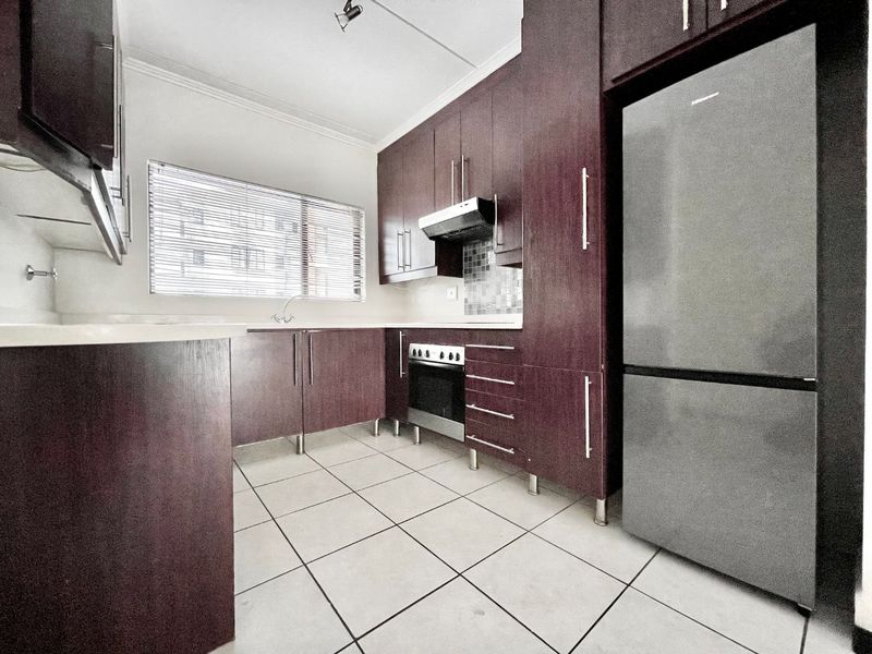 A functional kitchen featuring dark wood cabinetry, built-in oven, extractor fan, mosaic backsplash, and tiled flooring.