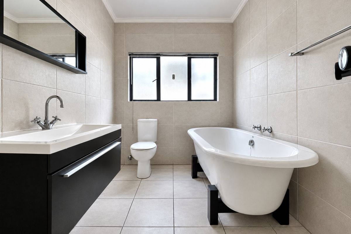 Modern bathroom featuring a freestanding bathtub, wall-mounted vanity with basin, toilet, and neutral floor-to-ceiling tiling.
