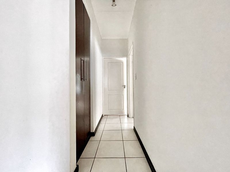 A clean, empty hallway featuring tiled flooring and a built-in storage cupboard, providing access to adjacent rooms.