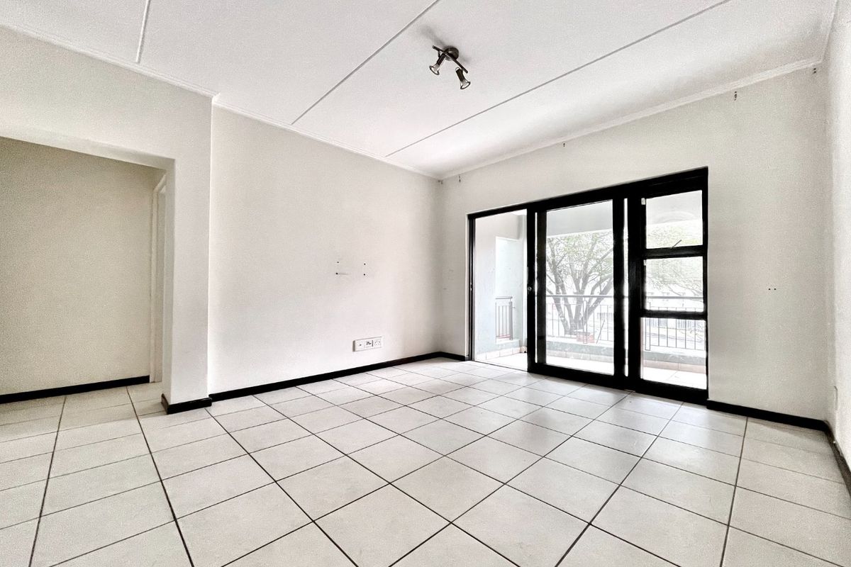An empty, well-lit living room featuring neutral tiled flooring and a large sliding glass door providing access to an outdoor balcony area.