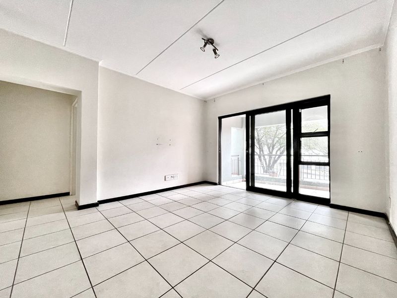 An empty, well-lit living room featuring neutral tiled flooring and a large sliding glass door providing access to an outdoor balcony area.