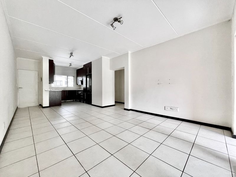 An open-plan living and kitchen area featuring neutral tiled flooring, dark built-in cabinetry, and a clean, minimalist layout ready for furnishing.