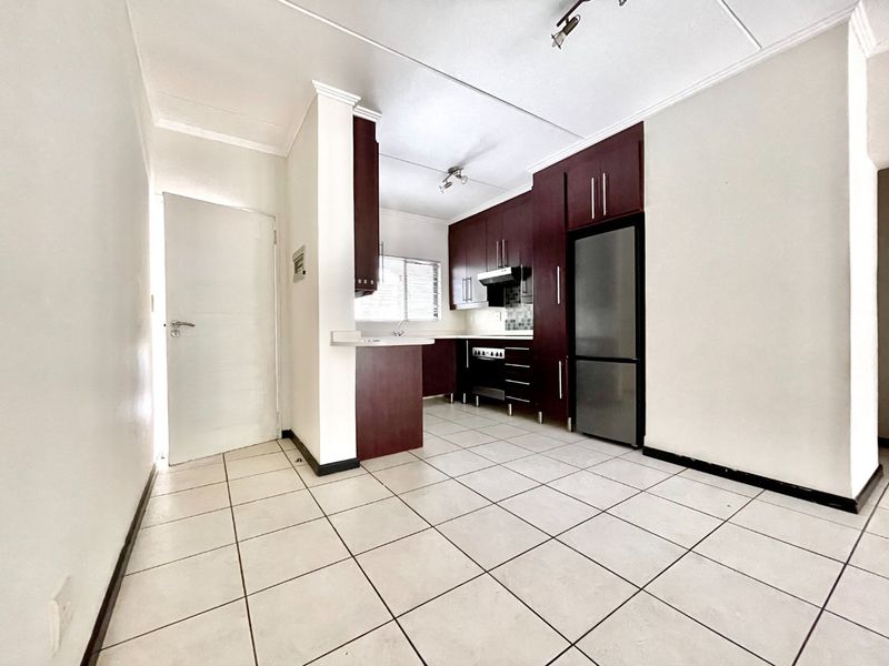A clean, empty kitchen featuring dark wood cabinetry, built-in oven, extractor fan, and tiled flooring with a functional breakfast counter layout.