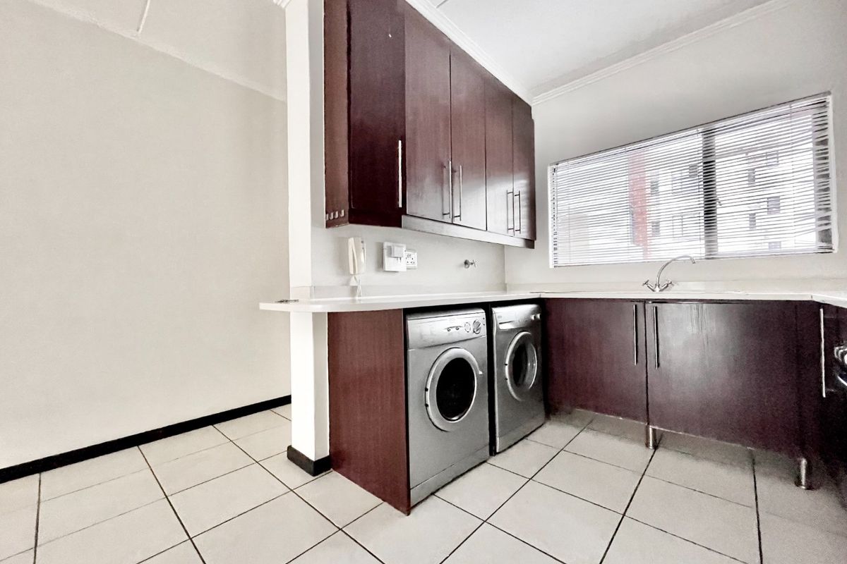 A functional kitchen featuring dark wood cabinetry, laminate countertops, a stainless steel sink, and tiled flooring with space for laundry appliances.