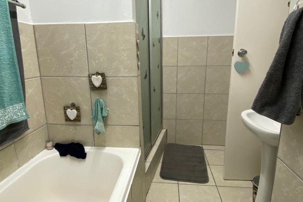 A functional bathroom featuring a bathtub, a separate shower enclosure with glass doors, and a pedestal basin with neutral ceramic wall and floor tiling.