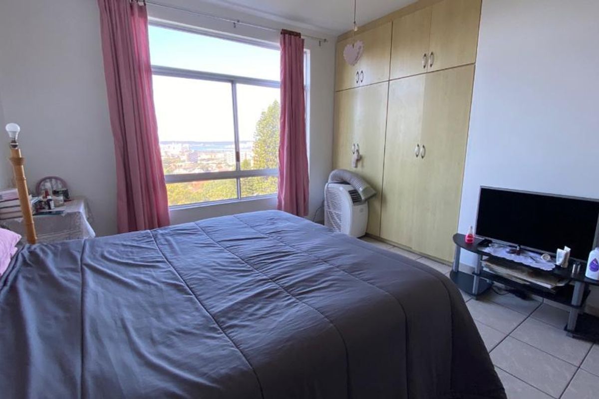A bedroom featuring built-in cupboards, tiled flooring, and a large window offering natural light and elevated views.