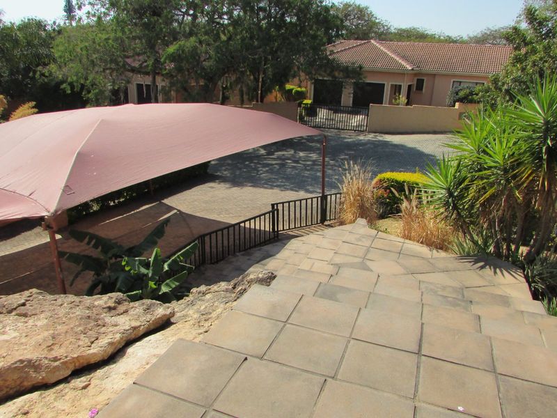Exterior view of the property entrance featuring a paved driveway, shade sail parking area, and tiled staircase leading down to the residence.