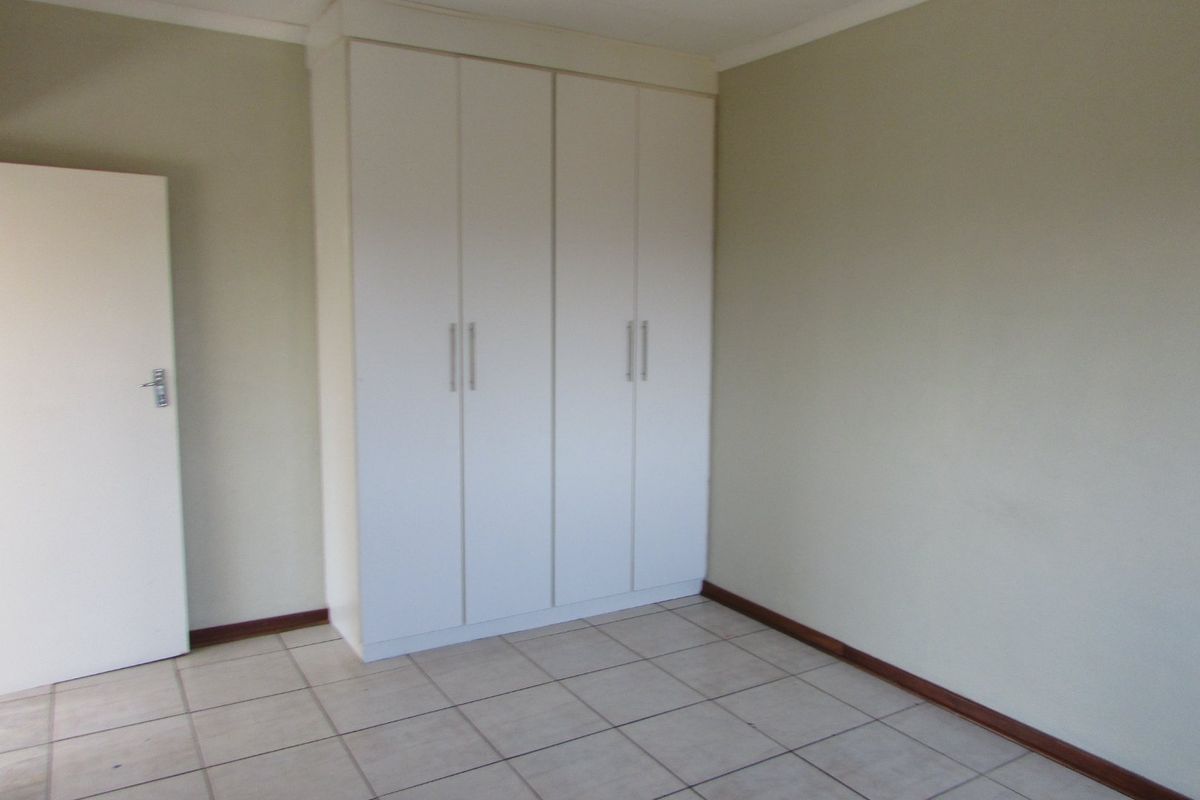 A clean, empty bedroom featuring neutral walls, tiled flooring, and a built-in wardrobe with white cabinetry.