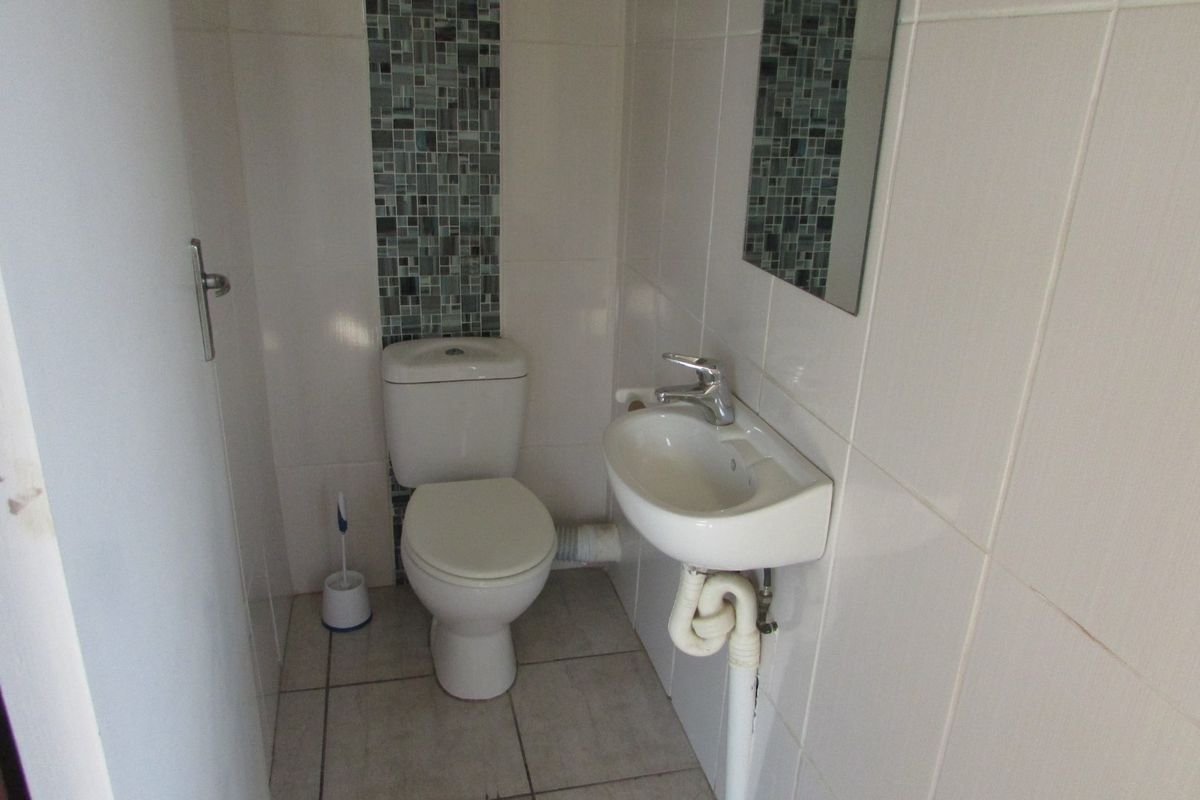 A compact guest bathroom featuring a wall-mounted basin, toilet, and neutral wall tiling with a decorative mosaic accent strip.