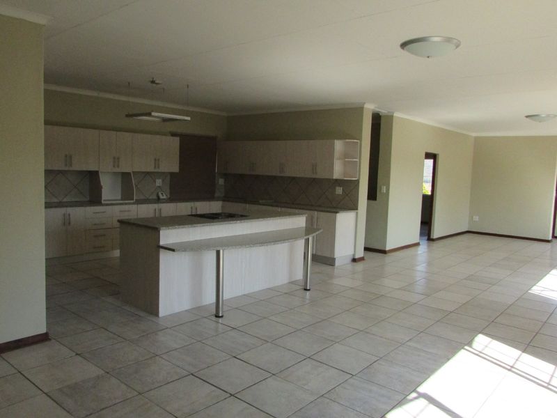 Spacious open-plan living area featuring a large kitchen with built-in cabinetry, a central island with a hob, and neutral tiled flooring throughout.