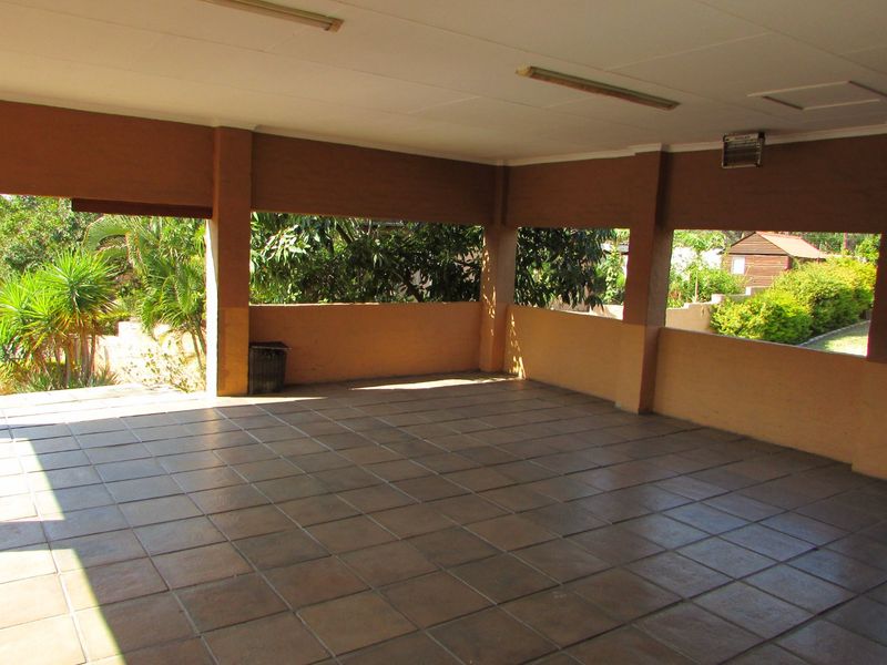 A spacious, covered outdoor patio area featuring tiled flooring and masonry pillars, offering a versatile space for outdoor living and entertaining.