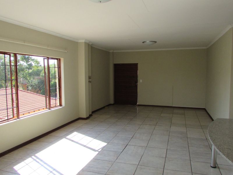 Spacious open-plan living area featuring neutral tiled flooring, a granite breakfast bar, and large windows providing natural light.