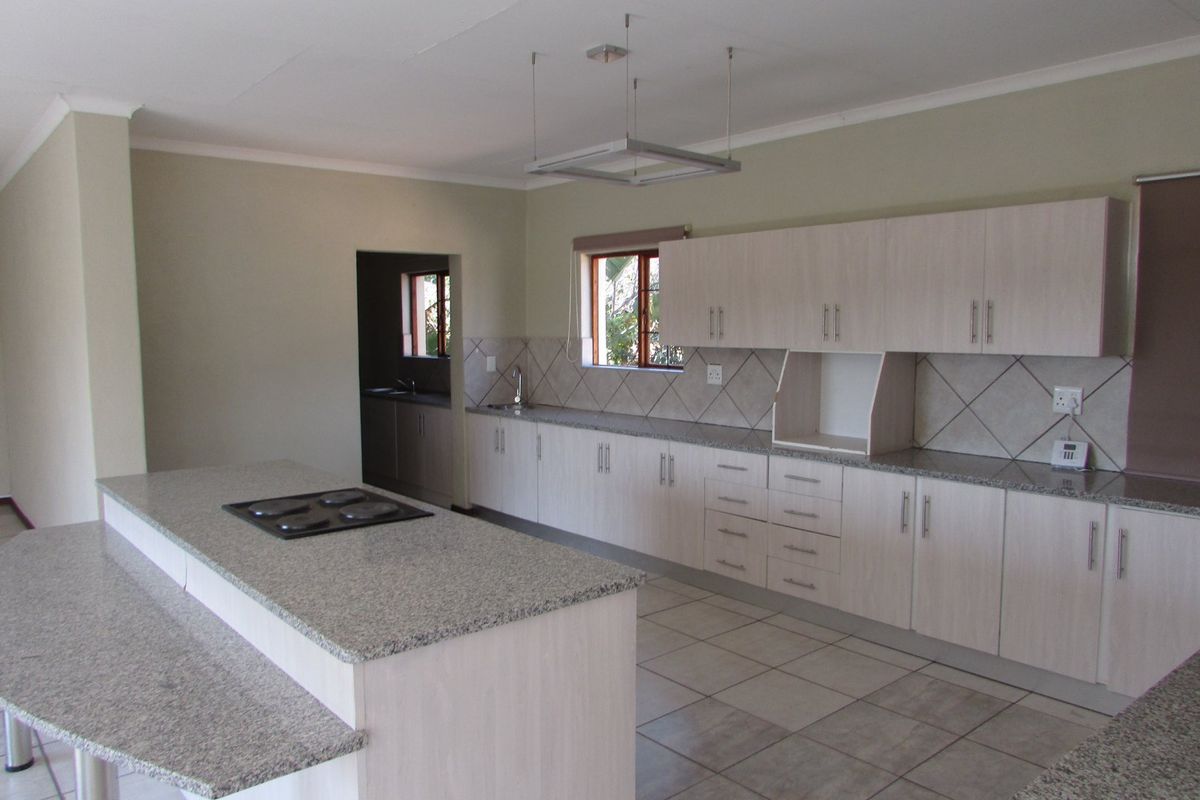 Spacious kitchen featuring light wood cabinetry, granite countertops, a central island with a built-in hob, and tiled flooring.