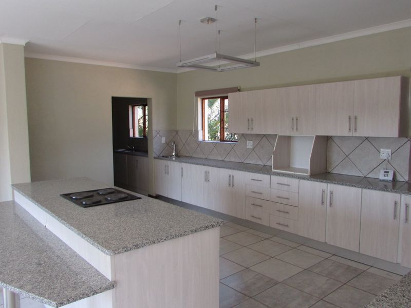 Spacious kitchen featuring light wood cabinetry, granite countertops, a central island with a built-in hob, and tiled flooring.