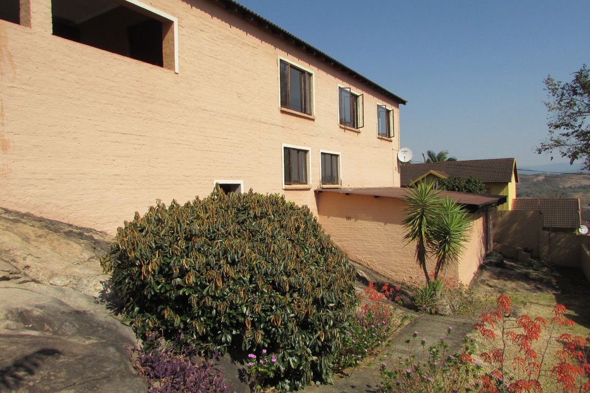 Rear exterior view of the townhouse featuring a painted brick facade, multiple casement windows, and a flat roof extension over a rocky garden area.