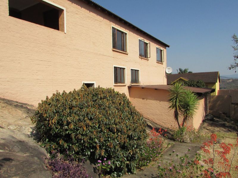 Rear exterior view of the townhouse featuring a painted brick facade, multiple casement windows, and a flat roof extension over a rocky garden area.