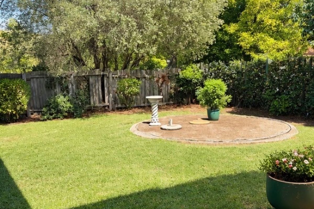A private backyard garden featuring a well-maintained lawn, a circular paved feature area, and established perimeter timber fencing.
