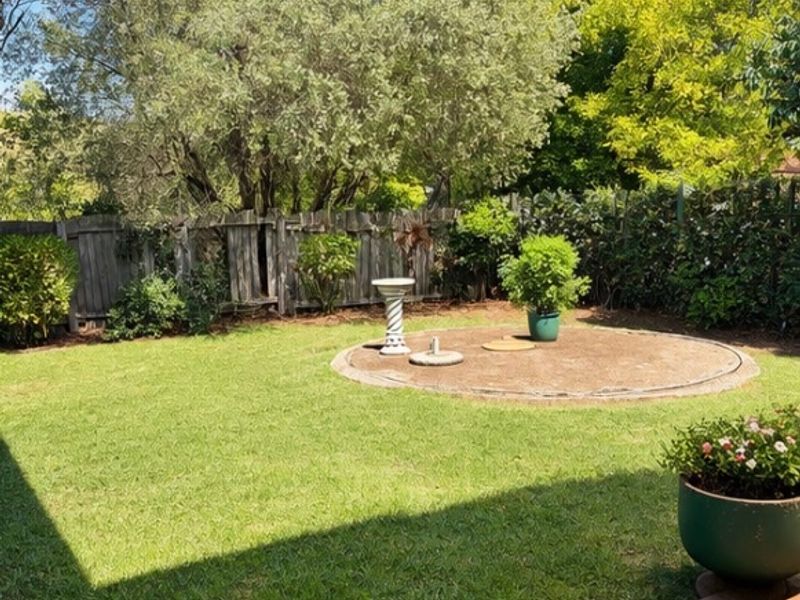 A private backyard garden featuring a well-maintained lawn, a circular paved feature area, and established perimeter timber fencing.